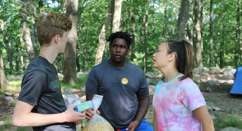 Three students speak to each other in a wooded area 